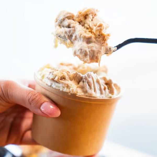 A hand holds a brown cup of creamy dessert, with a spoonful being lifted out.
