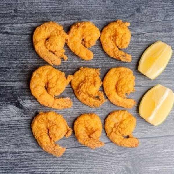 Nine golden-brown fried shrimp and two lemon wedges arranged on a dark wooden surface.