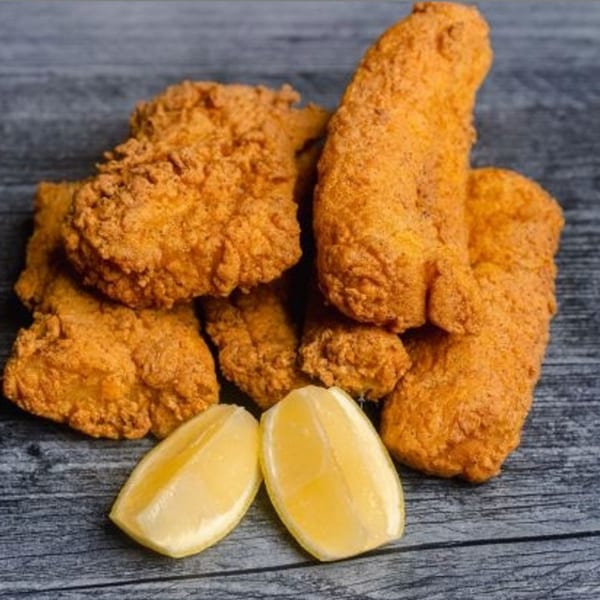 Crispy fried chicken pieces and two lemon wedges on a rustic wooden surface.