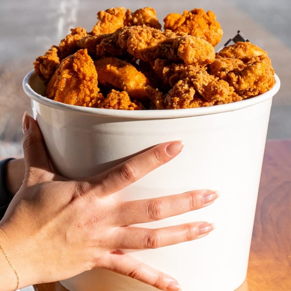 A hand holds a large white bucket overflowing with golden-brown fried chicken pieces from Uncle C's.