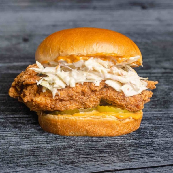 Uncle C's fried chicken sandwich with coleslaw, pickles, and sauce on a brioche bun.