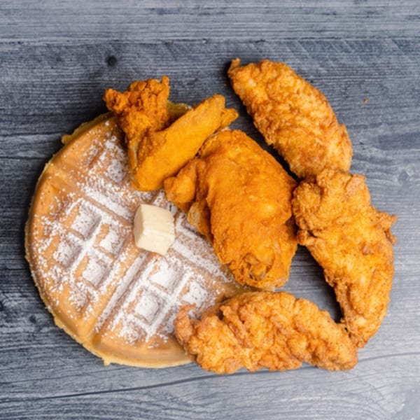 Golden fried chicken pieces and a waffle with powdered sugar and butter on a wooden surface.