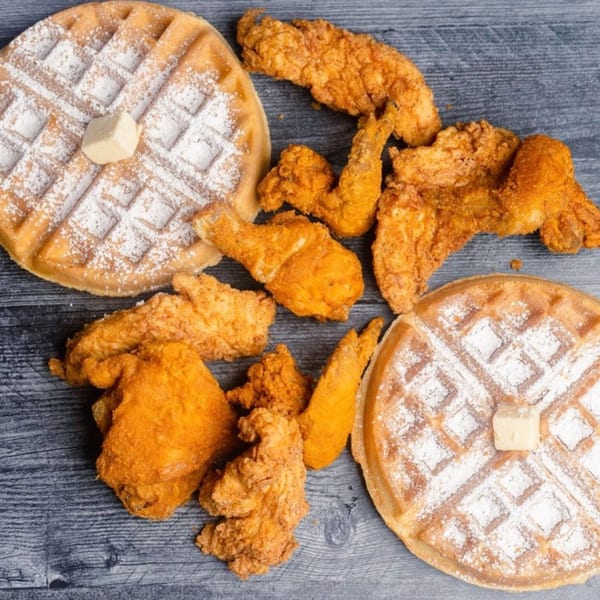 Golden fried chicken pieces and two powdered sugar waffles with butter on a dark wooden surface.