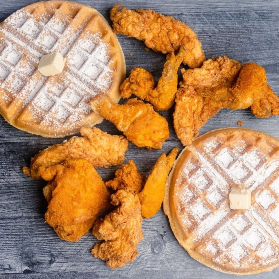 Golden fried chicken pieces and two powdered sugar waffles with butter on a dark wooden surface.